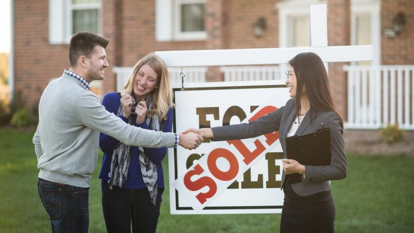 husband and wife are standing outdoors in front of their new house