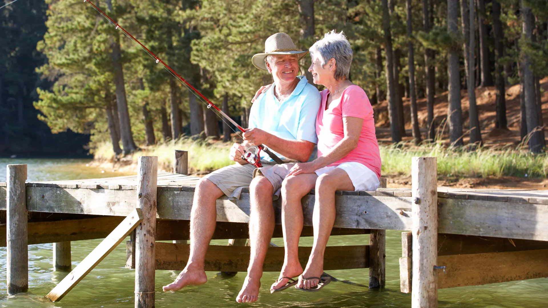 Senior couple sitting on jetty together fishing.