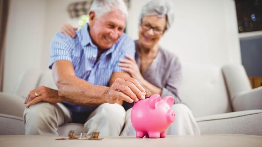 senior old retired couple putting coin into piggy bank