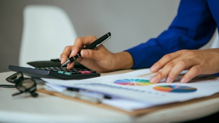 close up of hands holding pen using calculator pointing to stock chart