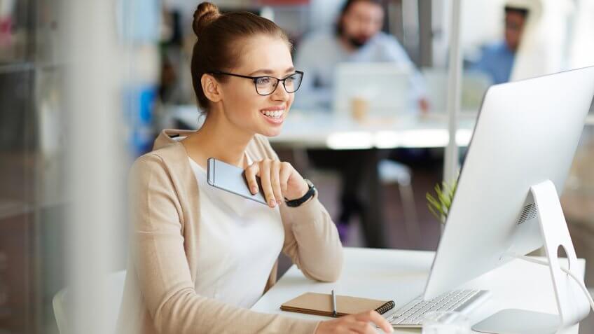 woman looking happily at her computer holding her phone