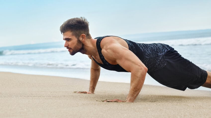 man doing a push up on the beach