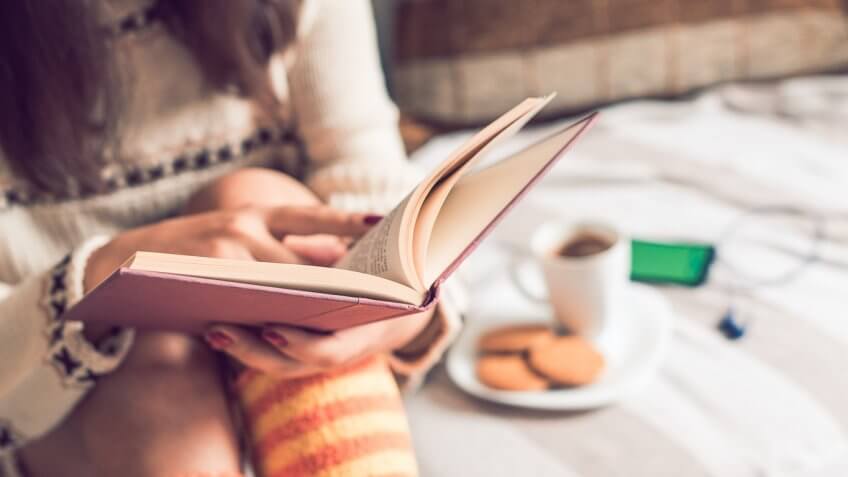 person reading a book next to cookies and coffee
