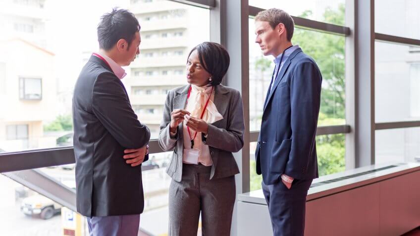International businesspeople are talking at hallway of office building.