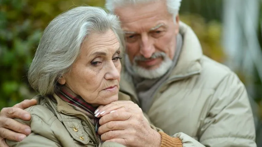 senior old couple holding each other looking sad