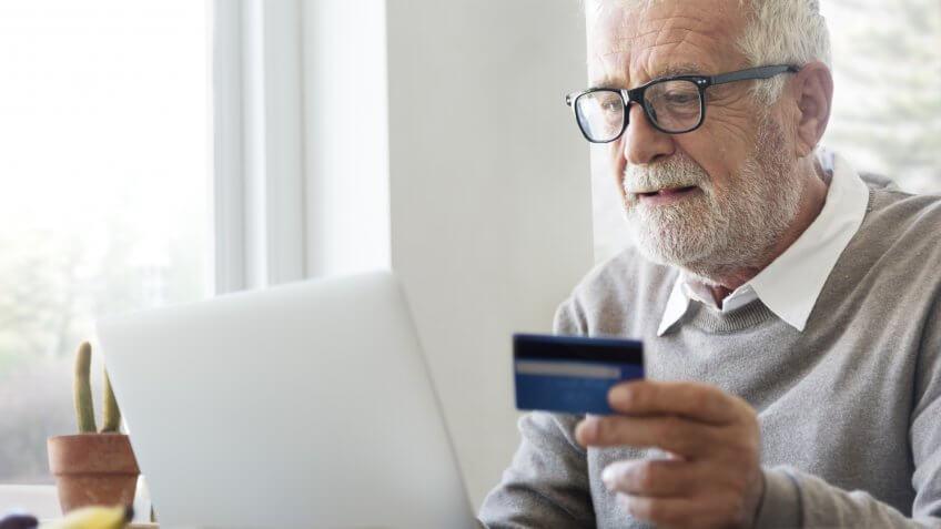 old senior man holding credit card typing on laptop
