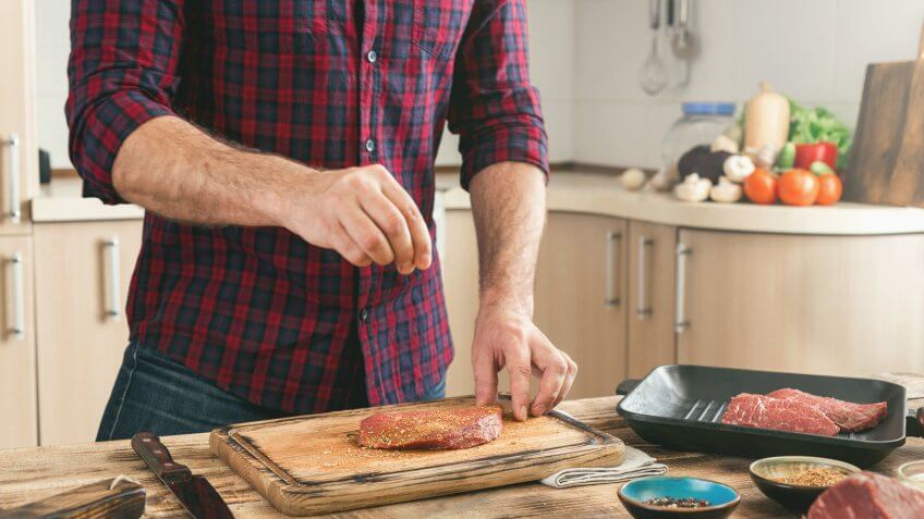man seasoning raw meat in the kitchen