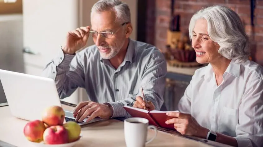 old senior couple together on laptop and writing