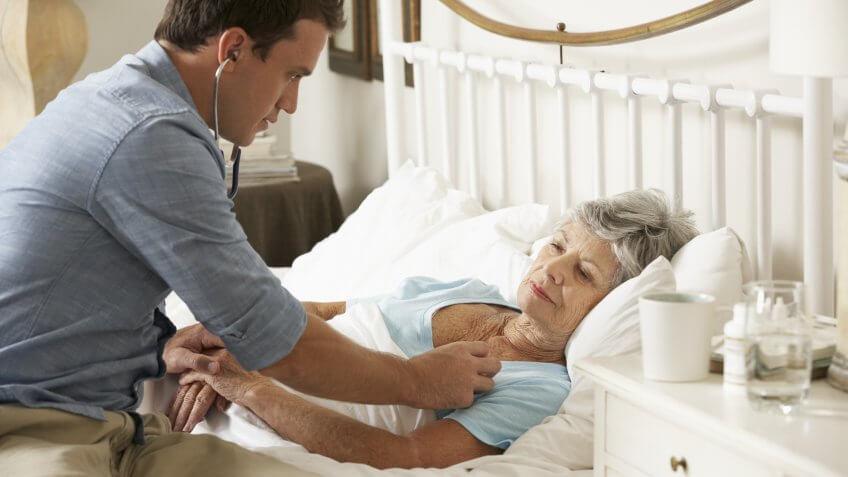 doctor with stethoscope to old senior retired woman in her home bed