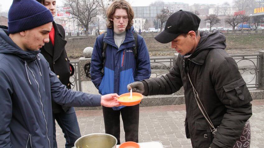 man giving soup to another man outside soup kitchen