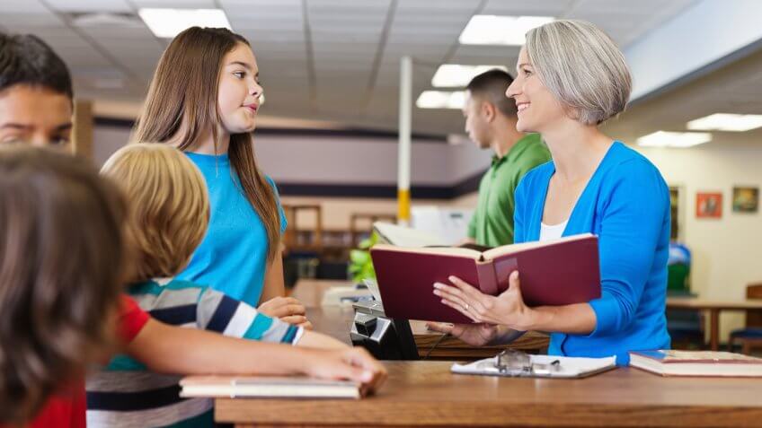 Librarian teacher helping students check out books in school libraryhttp://www.
