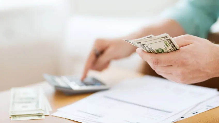 person holding money typing into a calculator