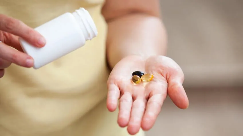woman dumping health supplements into her hand out of a pill bottle