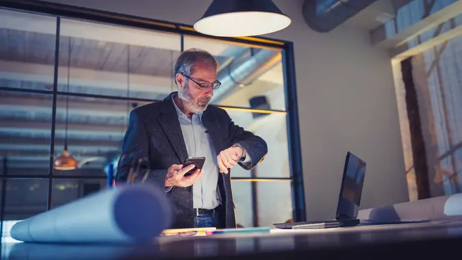 Senior adult architect working late in his design studio, using mobile phone.