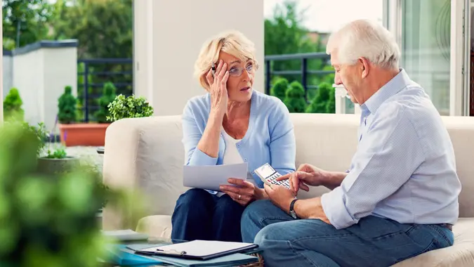 A senior couple sitting outside and worried about their finances, retirement plans and other money woes.