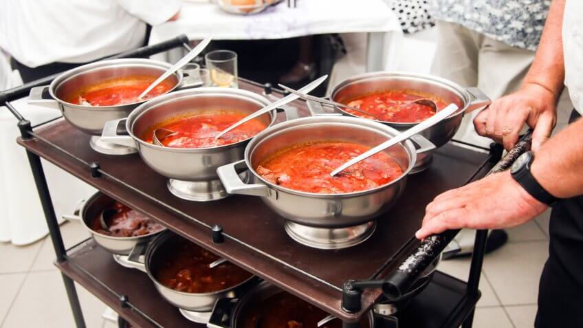 Hungarian goulash served in bowls on a serving cart pushed by waiter.