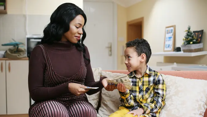 A mom sitting with her son at home, handing him cash