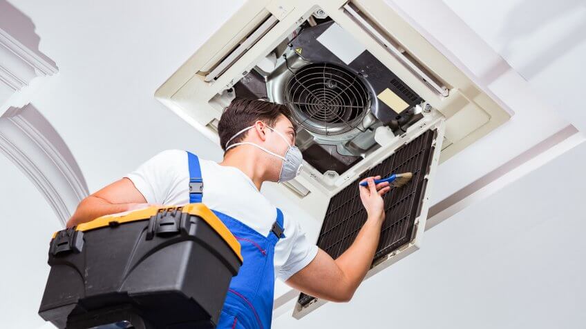 22 Industries That Pay Less (and More) Than They Did 10 Years Ag, Worker repairing ceiling air conditioning unit