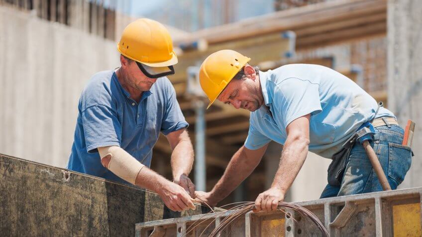 22 Industries That Pay Less (and More) Than They Did 10 Years Ag, Construction workers collaborating in the installation of cement