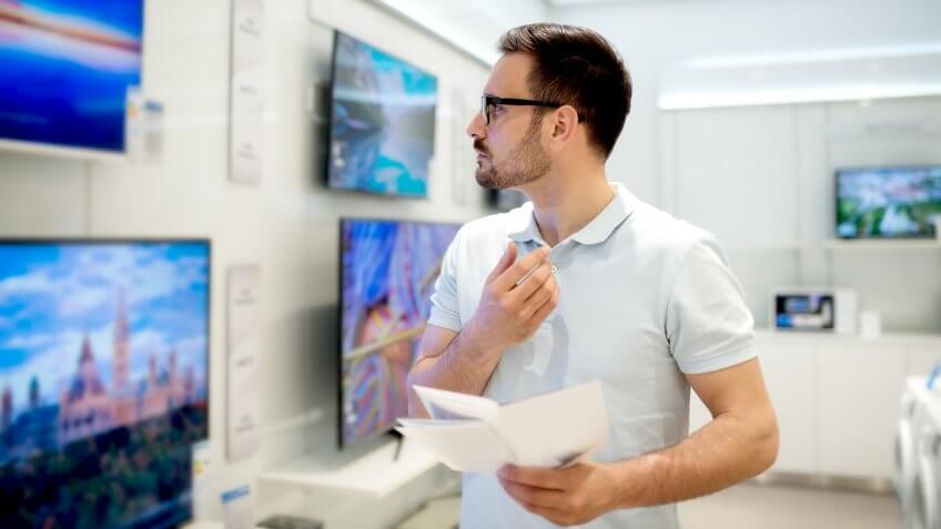 Handsome young man reading the use instructions. Buying new tv s, The Best and Worst Things to Buy in August 2017
