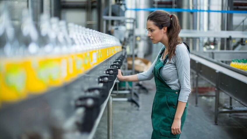 22 Industries That Pay Less (and More) Than They Did 10 Years Ag, Female factory worker inspecting production line at drinks produ