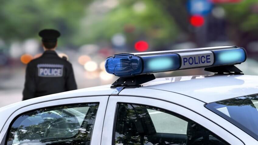 22 Industries That Pay Less (and More) Than They Did 10 Years Ag, Police officer emergency service car driving street with siren l