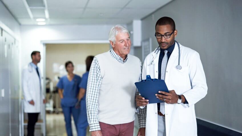 Cropped shot of a doctor talking to a senior patient while standing in the hospital corridor.