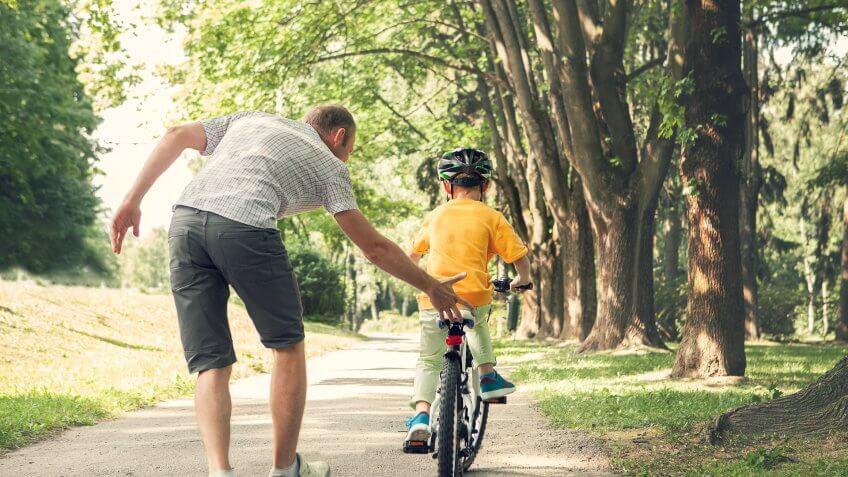 son with helmet riding bicycle with father