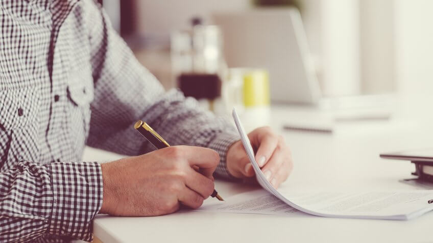 Man sitting at the table, holding a pen and signing contract.