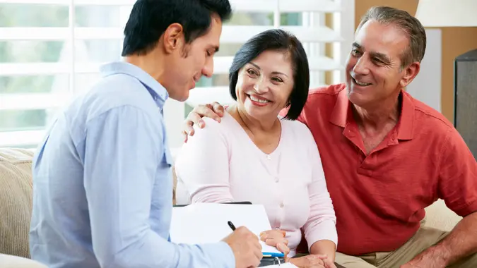 Financial Advisor Talking To Senior Couple At Home Writing Documents Smiling.