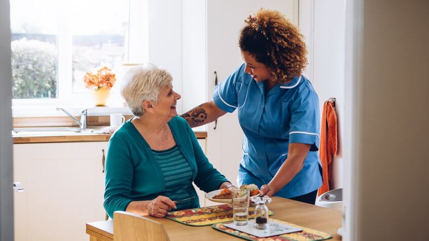 Care worker giving an old lady her dinner in her home.