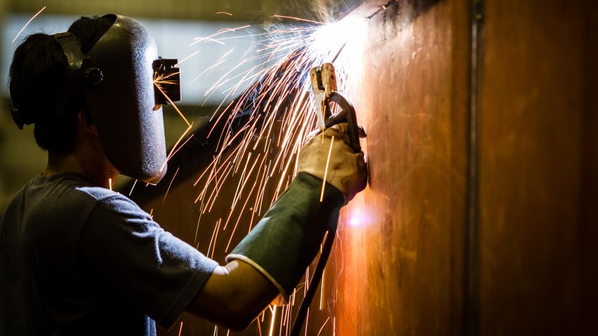 worker with protective mask welding metal and sparks