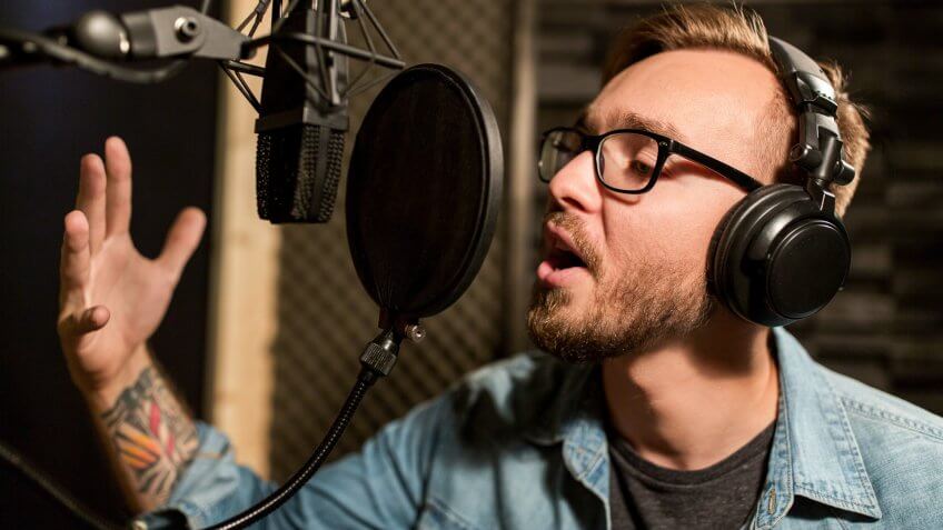 96 Money-Making Skills You Can Learn in Less Than a Year, Music, people and voice concept - male singer with headphones and micro, show business