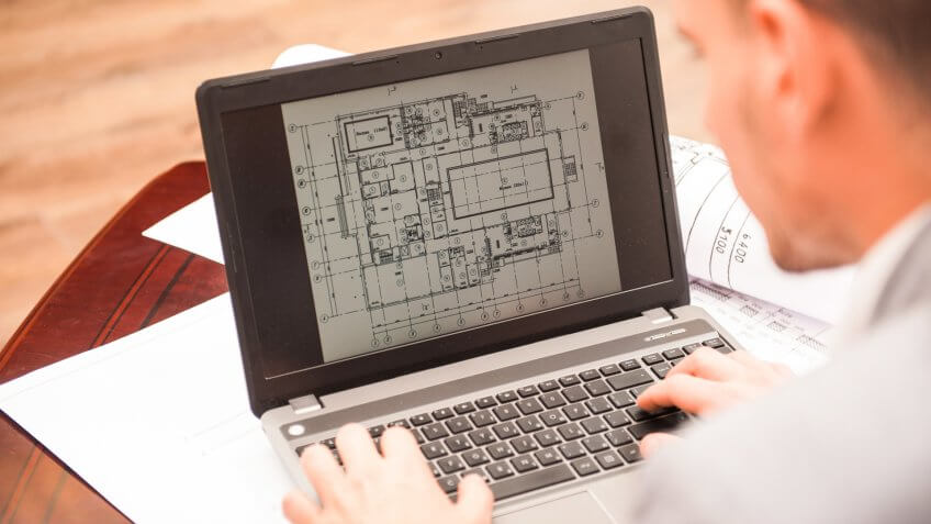 96 Money-Making Skills You Can Learn in Less Than a Year, Close-up portrait of laptop with blueprints, architect sitting from behind working on architectural plan, interior shot