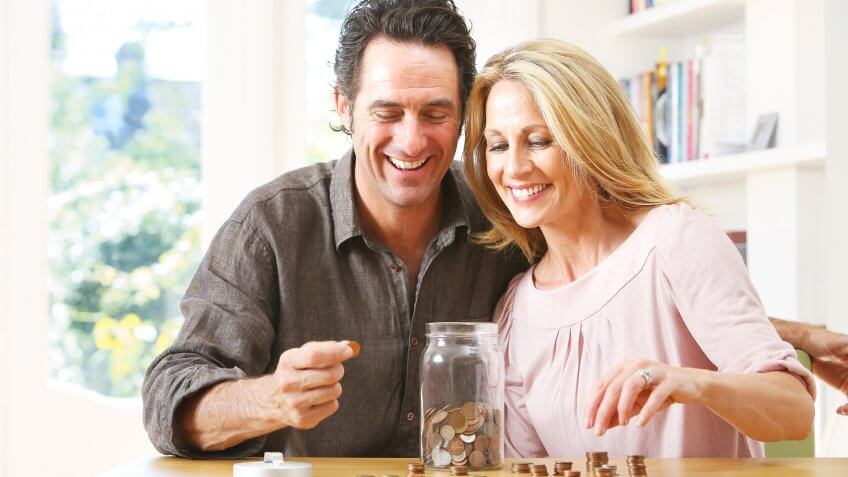 Middle aged couple counting coins into jar.