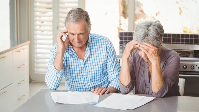 Worried senior couple with documents sitting in kitchen at home