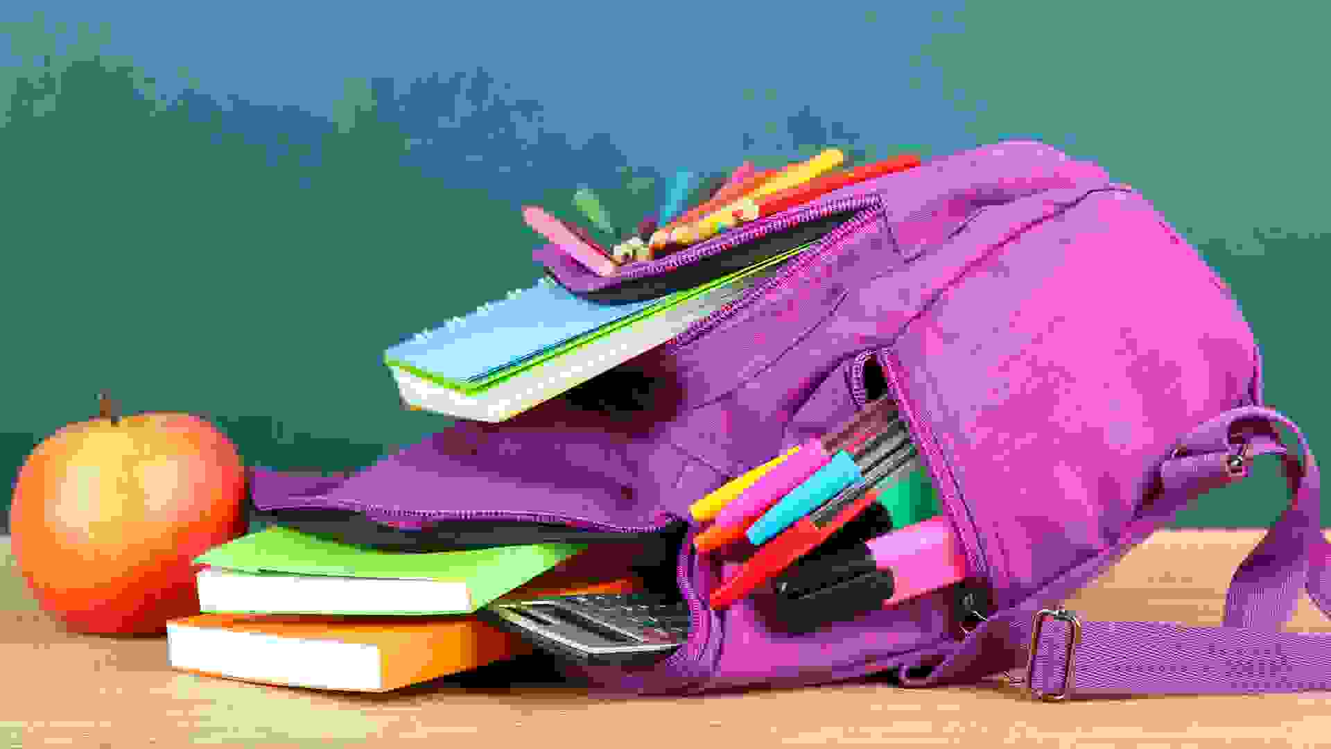 Purple backpack with school supplies on wooden table on green desk backgroundPurple backpack with school supplies on wooden table on green desk backgroundPurple backpack with school supplies on green desk background.