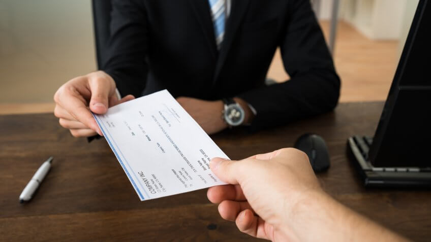 Close-up Of Businessman Hands Giving Cheque To Other Person In Office.