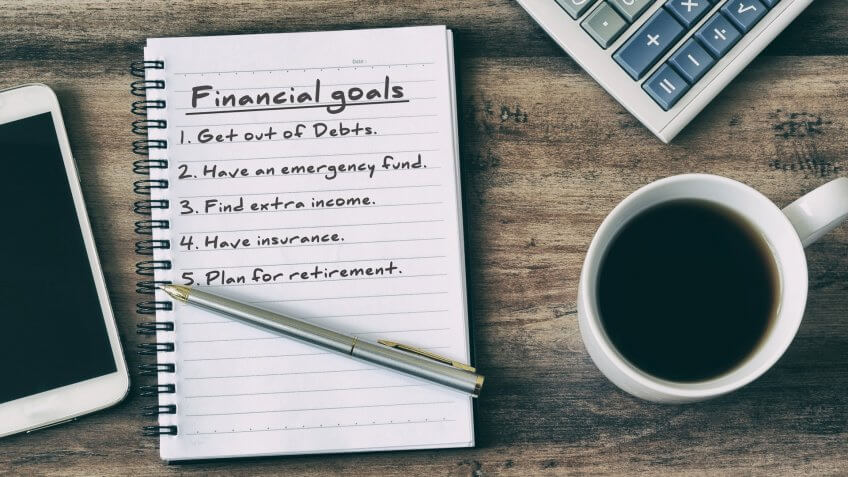Financial goals on notepad on blank notepad with calculator, Secret Tips to Live a Financially Secure Life, coffee, pen and smart phone on a wooden table, retro style.