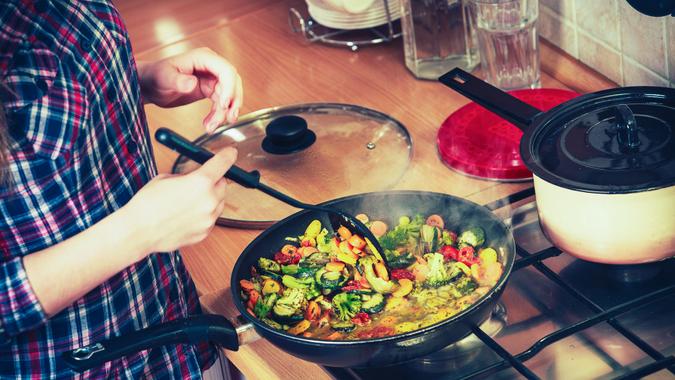 Closeup of human in kitchen cooking stir fry frozen vegetables.