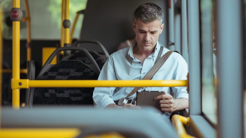 Businessman commuting to work by bus and working with a digital touch screen tablet.