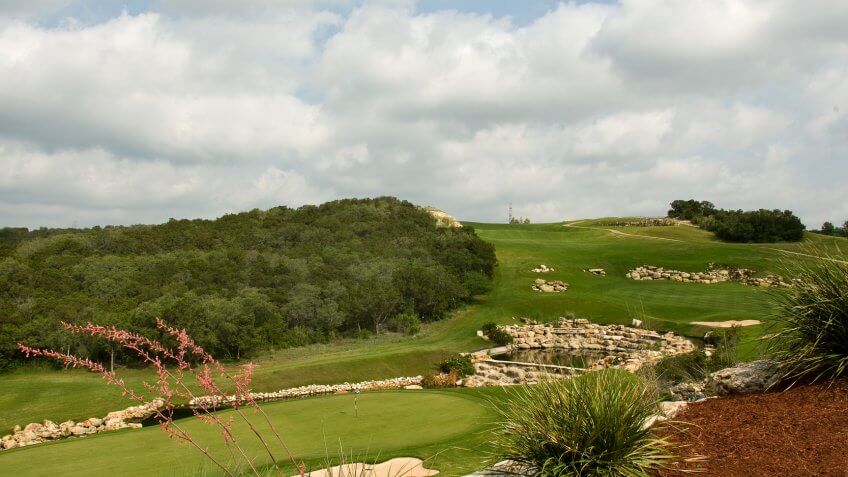 "photograph of La Cantera Golf Club, Palmer Golf Course, Hole 9, San Antonio, Texas, with fairway, putting green, Rocks, Ponds, flag, blue sky, trees".