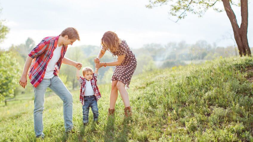 Photo of a young family enjoying holidays in the park on a sunny summer day near big family tree countryside.