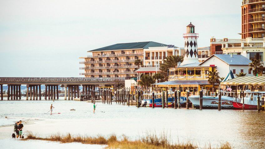 Destin, Florida, US - February 26, 2014: People enjoying a sandy beach at sunset time, Harborwalk Marina in background.