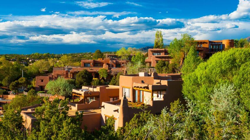 Hillside houses and trees in Santa Fe, New Mexico, with clouds in the background.
