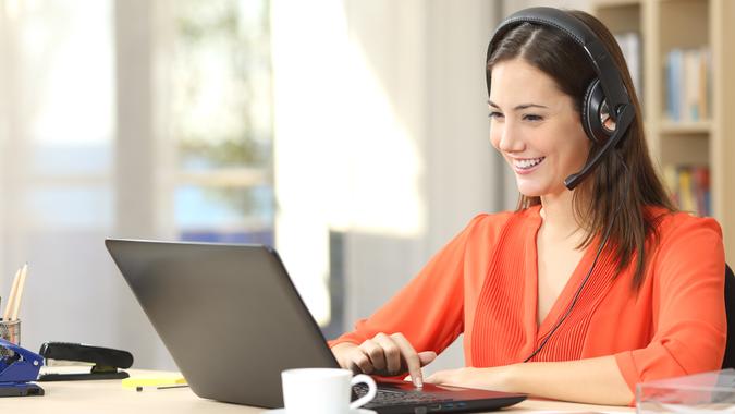 Beautiful freelancer female talking in a video conference on line with a headset with microphone and laptop in an office desktop or home desk