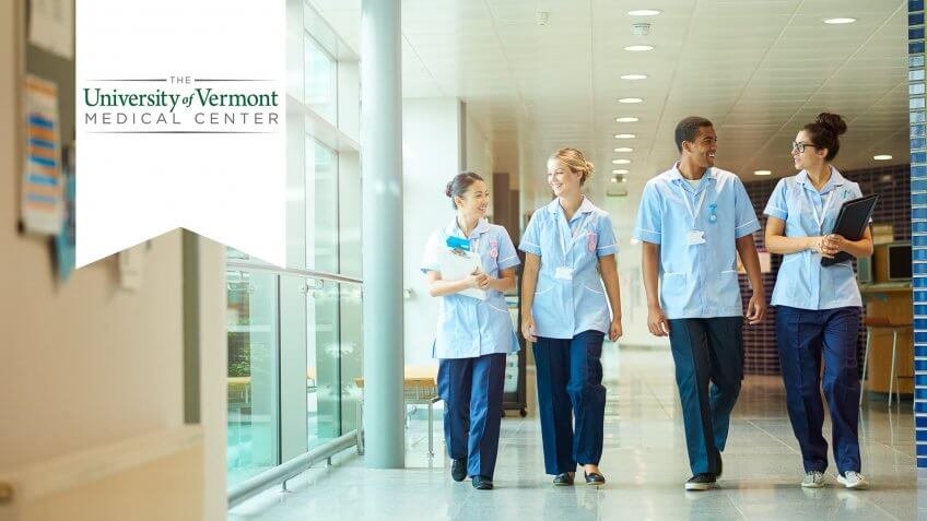 a group of four young trainee nurses including male and female nurses , walk towards camera down a hospital corridor .
