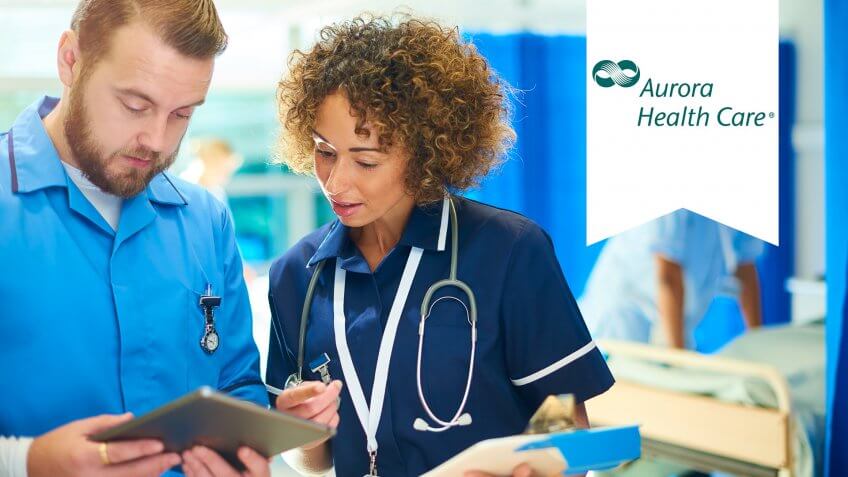 a nursing sister stands with a male nurse chatting about the medical chart that she is holding and cross referencing it with the digital tablet that he is holding.