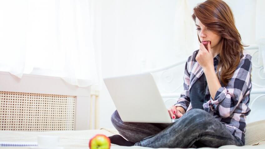 Young woman using laptop while sitting on bed.