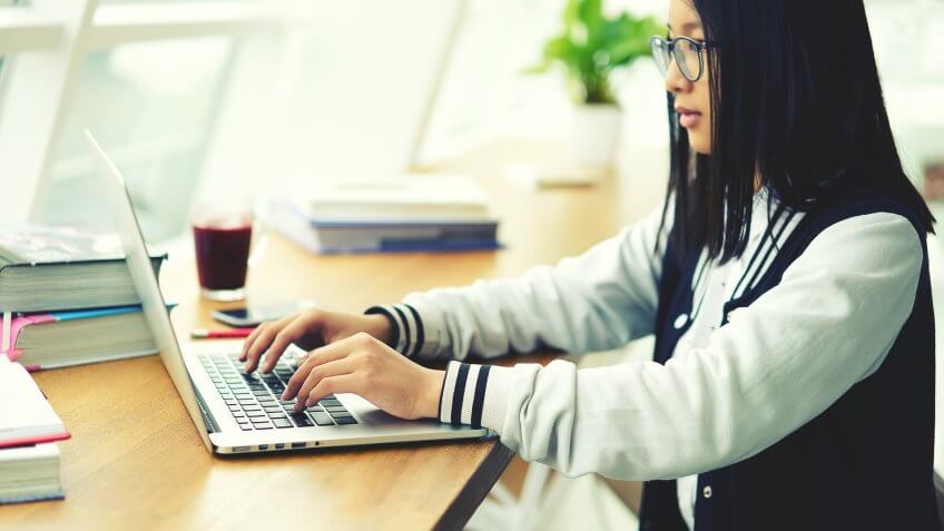 teenager keyboarding text message in social networks on computer using internet connection sitting in library.Young chinese student searching information on school websites